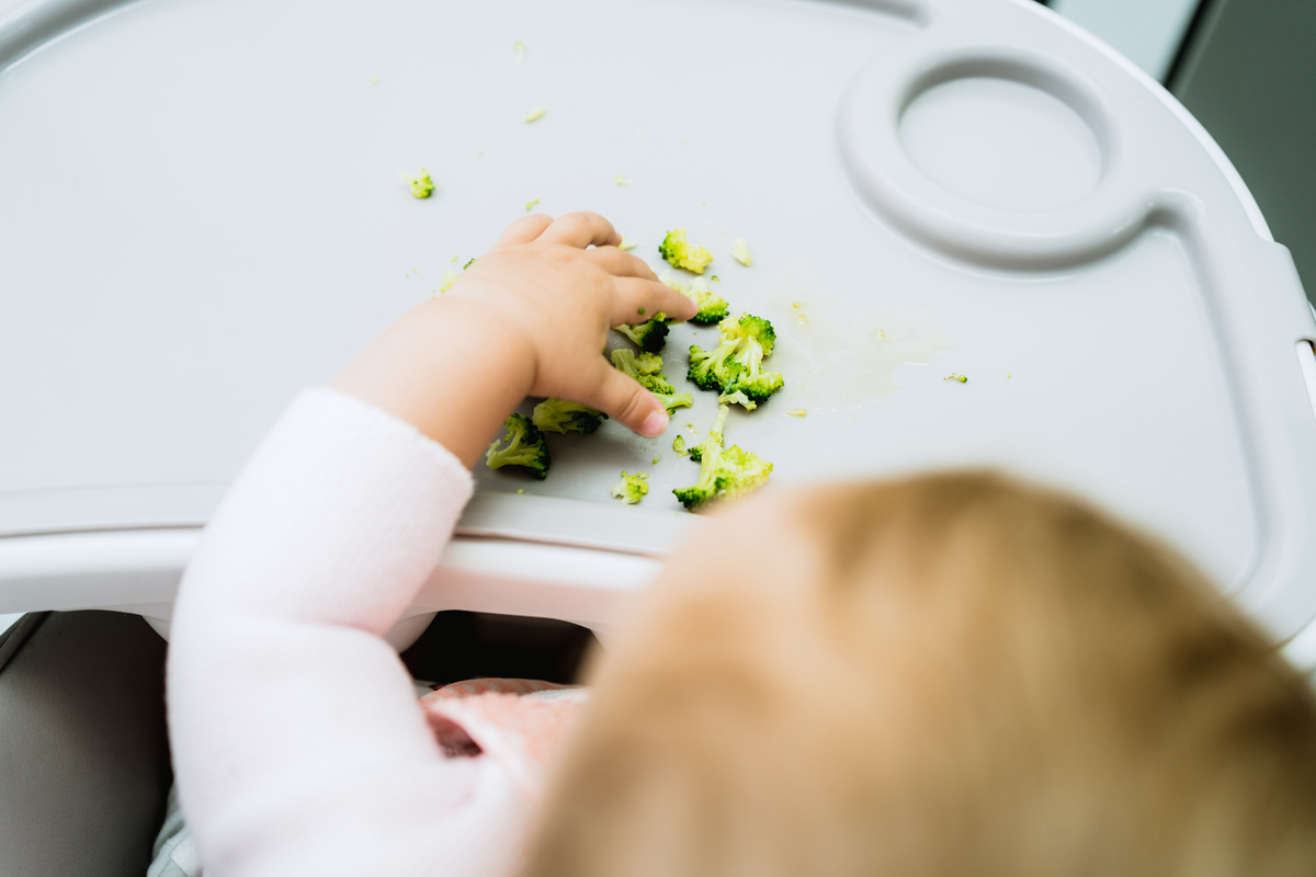 baby eating broccoli in early stages of baby-led weaning